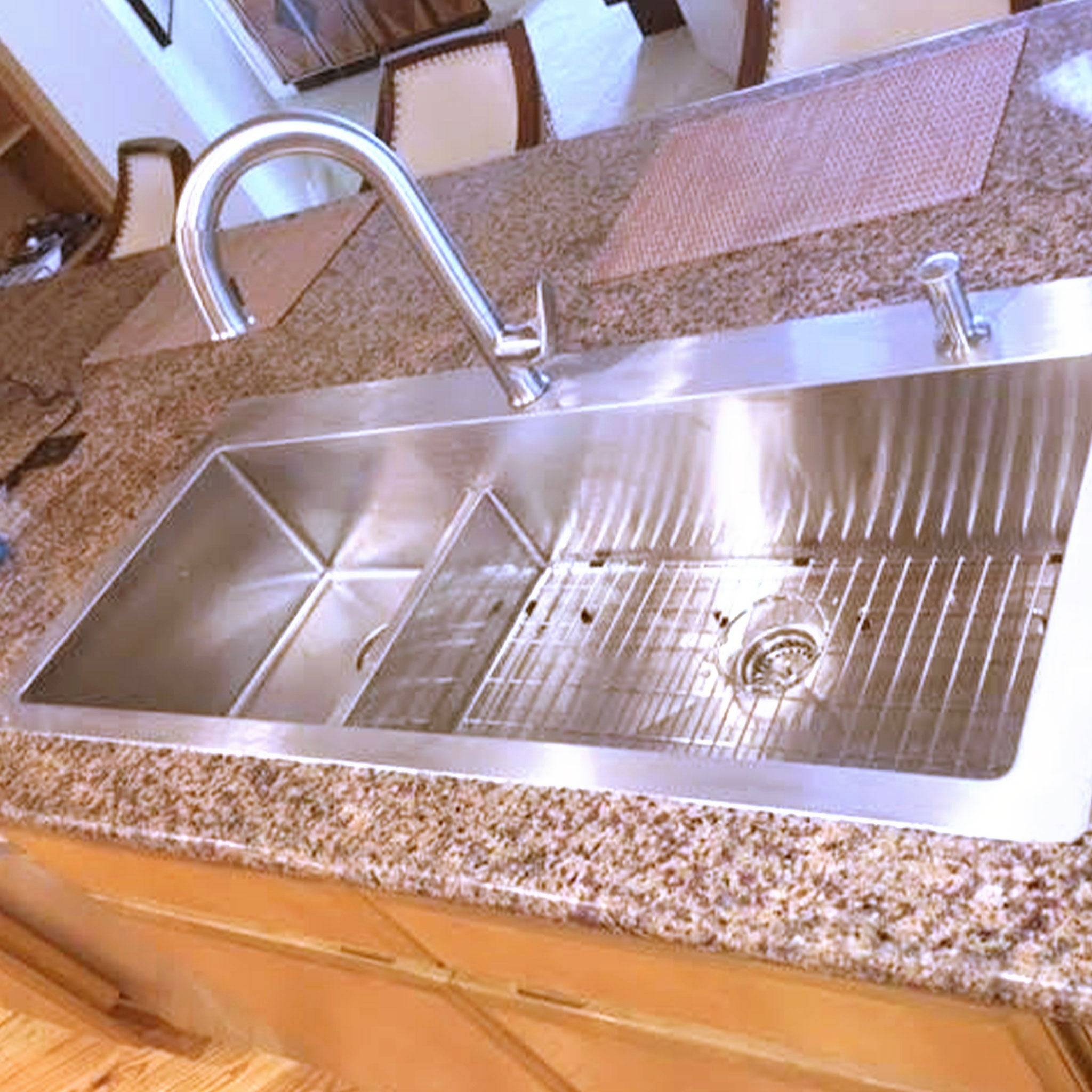 Installed 49-inch top mount drop-in double bowl sink with large right bowl in a granite countertop, featuring a high-arc faucet. Model TMD49.